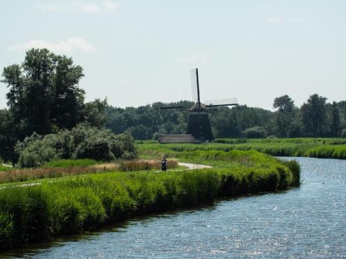 a person standing next to a river with a windmill at Holiday Home in Zevenhuizen with Sauna Bubble Bath in Zevenhuizen