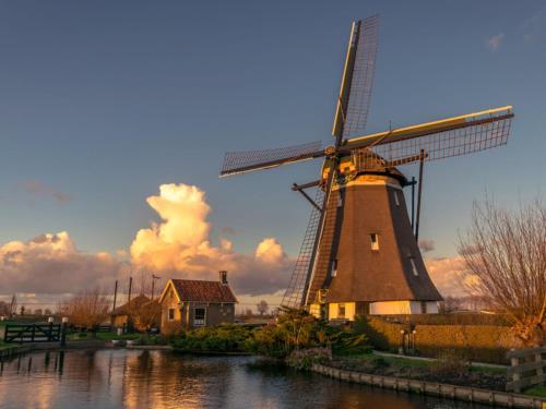 a windmill sitting in the water next to a house at Deluxe Canal-Side Stay in Zevenhuizen