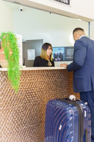 a man and a woman standing at a counter with a suitcase at Ibis Styles Invercargill in Invercargill