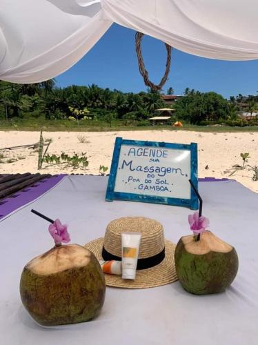 una mesa con dos cocos y un cartel en una playa en Belissima Suite frente ao mar, Praia Linda Gamboa, en Cayru