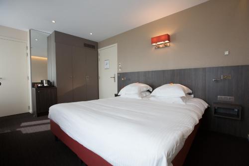 a large bed with white sheets and pillows on it at Albion Hotel in Ieper
