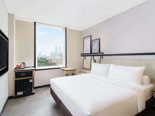 a bedroom with a large white bed and a window at ibis Jakarta Raden Saleh in Jakarta