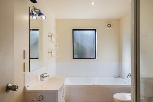 La salle de bains est pourvue d'une baignoire, d'un lavabo et de toilettes. dans l'établissement Relax on Queens - Waikanae Beach Holiday Home, à Waikanae