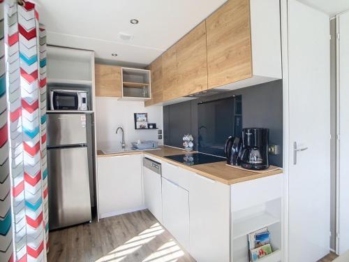 une cuisine avec des armoires blanches et un réfrigérateur en acier inoxydable dans l'établissement Mobil-Home Grand Confort 4 Pers. à 200m de la plage avec piscine chauffée et parking - FR-1-361A-15, à Jullouville