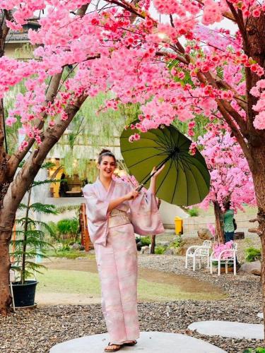 a woman holding an umbrella under a tree with pink flowers at Pupah Kanna Pua-ปู๋ ป๋าล์ คันนา ปัว in Pua