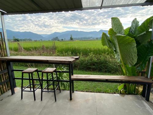 a bench and two stools on a porch with a field at DeeTorJai FarmStay Nan ดีต่อใจ ฟาร์มสเตย์ น่าน โดยเจ้าของ in Ban Klang