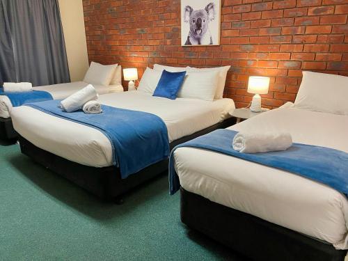 three beds in a room with a brick wall at City Heart Motel Warrnambool in Warrnambool