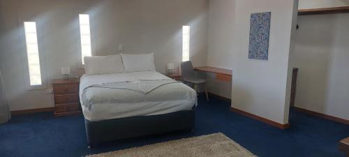a bedroom with a bed and a desk and two windows at Wilmots on Dixon in Alice Springs