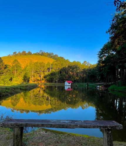a wooden bench sitting next to a lake with a house at Hotel Fazenda Rancho Mineiro in Engenheiro Paulo de Frontin