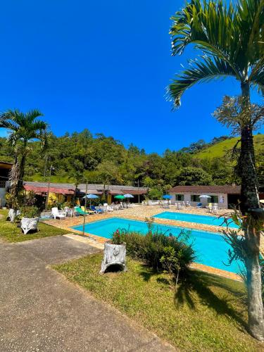 a swimming pool with a palm tree next to a resort at Hotel Fazenda Rancho Mineiro in Engenheiro Paulo de Frontin