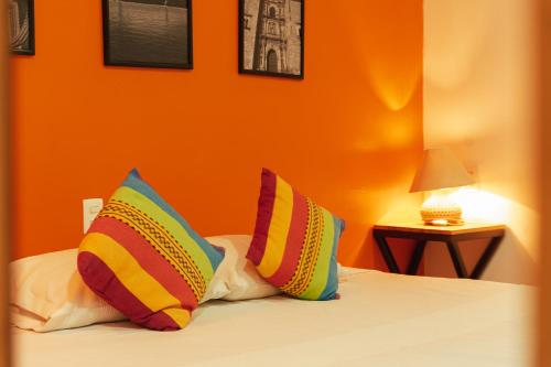a bed with colorful pillows on it with an orange wall at Casa Don José: NARANJOS Suite in Oaxaca City