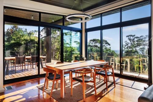 a dining room with a table and chairs and large windows at Sanctuaire, Southern Highlands in Mittagong