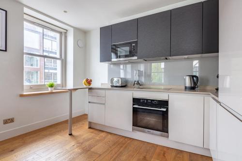 una cocina con armarios blancos y electrodomésticos de acero inoxidable en Central Fitzrovia - CityApartmentStay en Londres
