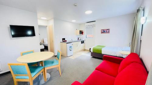 a room with a red couch and a table and a bed at Bella Vista Motel Whangarei in Whangarei