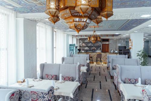 a restaurant with white tables and chairs and chandeliers at Jannat Resort Osh in Osh