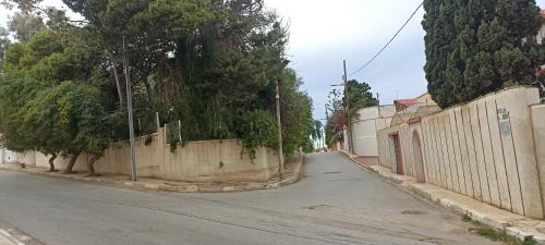 an empty street with a fence and trees on the side at Le Bon Coin in 'Aïn el Turk