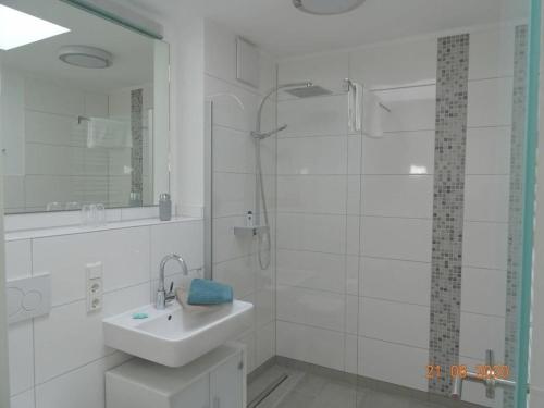 ein weißes Bad mit einem Waschbecken und einer Dusche in der Unterkunft Old Printing House Holiday Apartment Cicero in Norderney