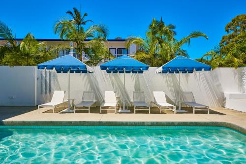 a group of chairs and umbrellas next to a swimming pool at The Sails Motel Brunswick Heads in Brunswick Heads