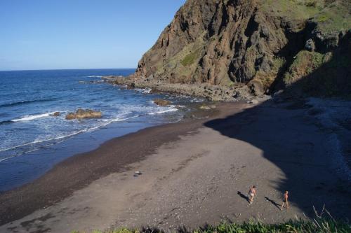 two people walking on a beach next to the ocean at Hotel Costa Linda in Porto da Cruz