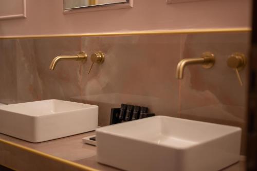 a bathroom with two white sinks and gold faucets at L Suites The Writer's House in Gythio