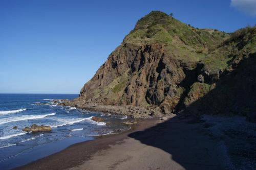 a beach with a rocky mountain and the ocean at Hotel Costa Linda in Porto da Cruz