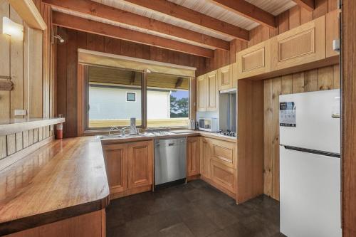 Una cocina con gabinetes de madera y un refrigerador blanco. en Sunset Dreams across the Sea, en Coronet Bay