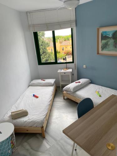 two beds in a room with a table and a window at Piso muy moderno para 4-5 personas a 7 min caminando a la playa, con aire, balcón con vistas y 2 piscinas in El Puerto de Santa María