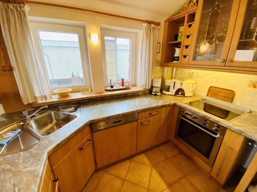 eine Küche mit Holzschränken, einem Waschbecken und 2 Fenstern in der Unterkunft Sonnenaufgang, direkt am Alten Strom in Warnemünde