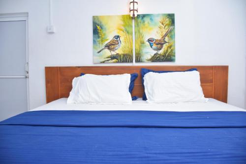 a bed with blue sheets and two paintings on the wall at French Garden Regish Guest House in Trincomalee