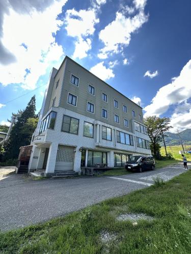a large white building with a car parked in front of it at Arise Hakuba Lodge in Nagano