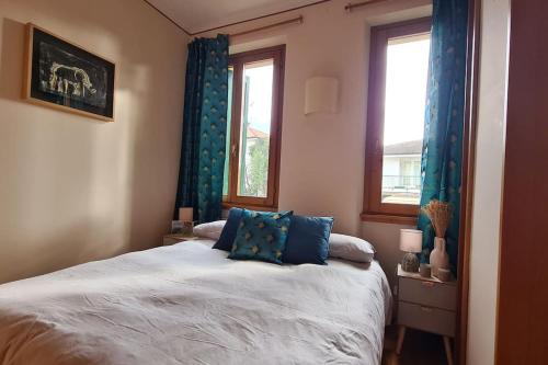 a bedroom with a bed with blue curtains and two windows at Il Nido di legno in Udine