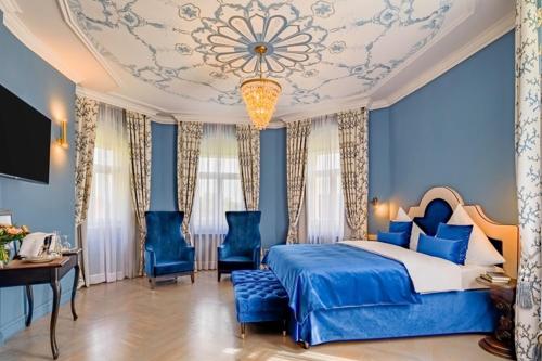 una camera da letto con letto, pareti blu e lampadario a braccio di Schloßhotel Althörnitz a Bertsdorf