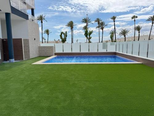 a swimming pool with green grass next to a building at Casa Virginia in Los Alcázares