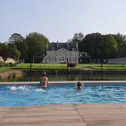 2 personnes dans une piscine avec une maison en arrière-plan dans l'établissement Chambres d'Hôtes Château de Martragny, à Martragny