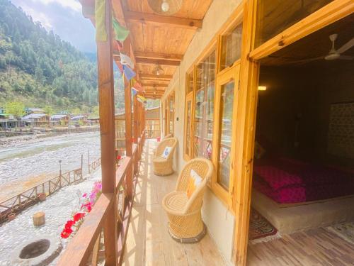 a porch of a house with wicker chairs on the beach at Living Good - A Himalayan Boutique Stay in Gushaini