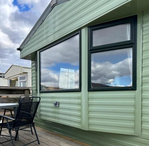 a green building with two windows and a table and a chair at Curacao Caravans in Taynuilt