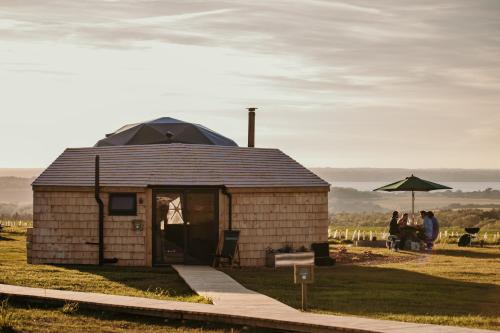 a small building in a field with people sitting under an umbrella at Dome Meadow 5 With Log Burning Tub At Tapnell Farm in Yarmouth