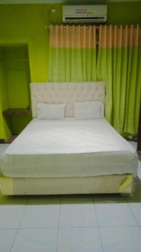 1 dormitorio con cama blanca y cortina verde en Hotel Grand Atlet Bengkulu en Bengkulu