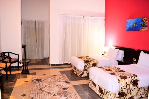 Cette chambre comprend 2 lits et un mur rouge. dans l'établissement Hostmark Zabargad Beach Resort, à Abū Ghuşūn