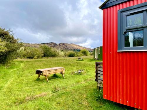 a red shed and a bench in a field at Shepherds Hut Glamping in Bantry