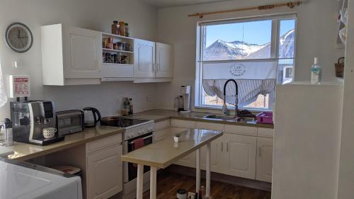 a kitchen with white cabinets and a window with a mountain at Flateyri guesthouse in Flateyri