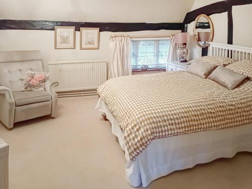 a bedroom with a bed and a chair and a mirror at Pipers Cottage in Beyton
