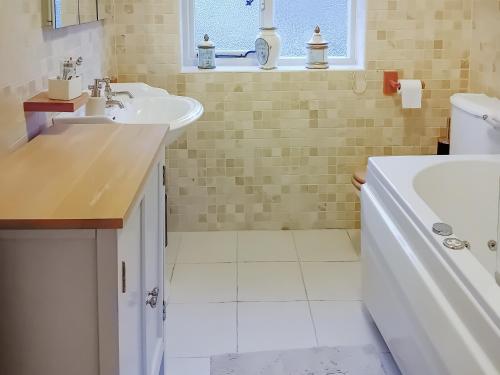 La salle de bains blanche est pourvue d'un lavabo et d'une baignoire. dans l'établissement Pipers Cottage, à Beyton
