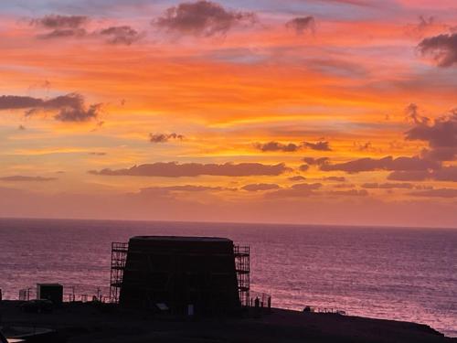 una puesta de sol sobre el océano con un edificio en la playa en Sirena Iris, en Cotillo