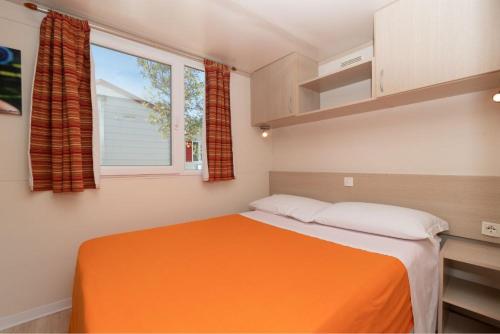 Un pequeño dormitorio con una cama naranja y una ventana en Camping Village VERDEMARE SRL, en Fermo