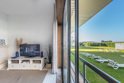a living room with a television and a balcony with chairs at GuestReady - Madalena Beach Pool & Tennis in Vila Nova de Gaia