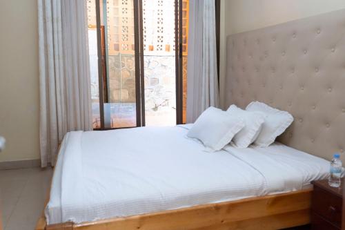 um quarto com uma cama com lençóis brancos e uma janela em Green V Apartments em Kigali