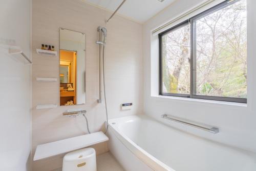 Oukai Villa Izumi في Izumi: حمام أبيض مع حوض استحمام ونافذة