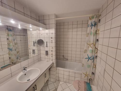a white tiled bathroom with a sink and a tub at Steiner Strandappartements Appartement 204 Seeseite in Stein