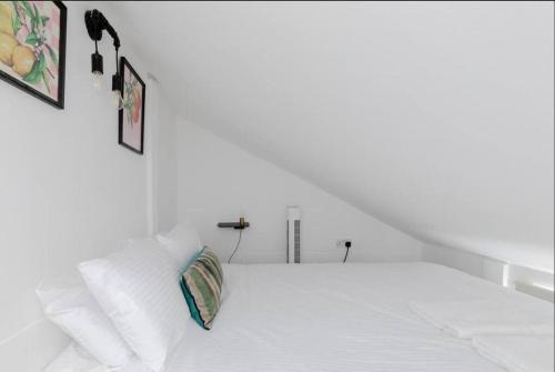 a white bed with white pillows and two pictures on the wall at Charming Primrose Hill Loft near train station in London